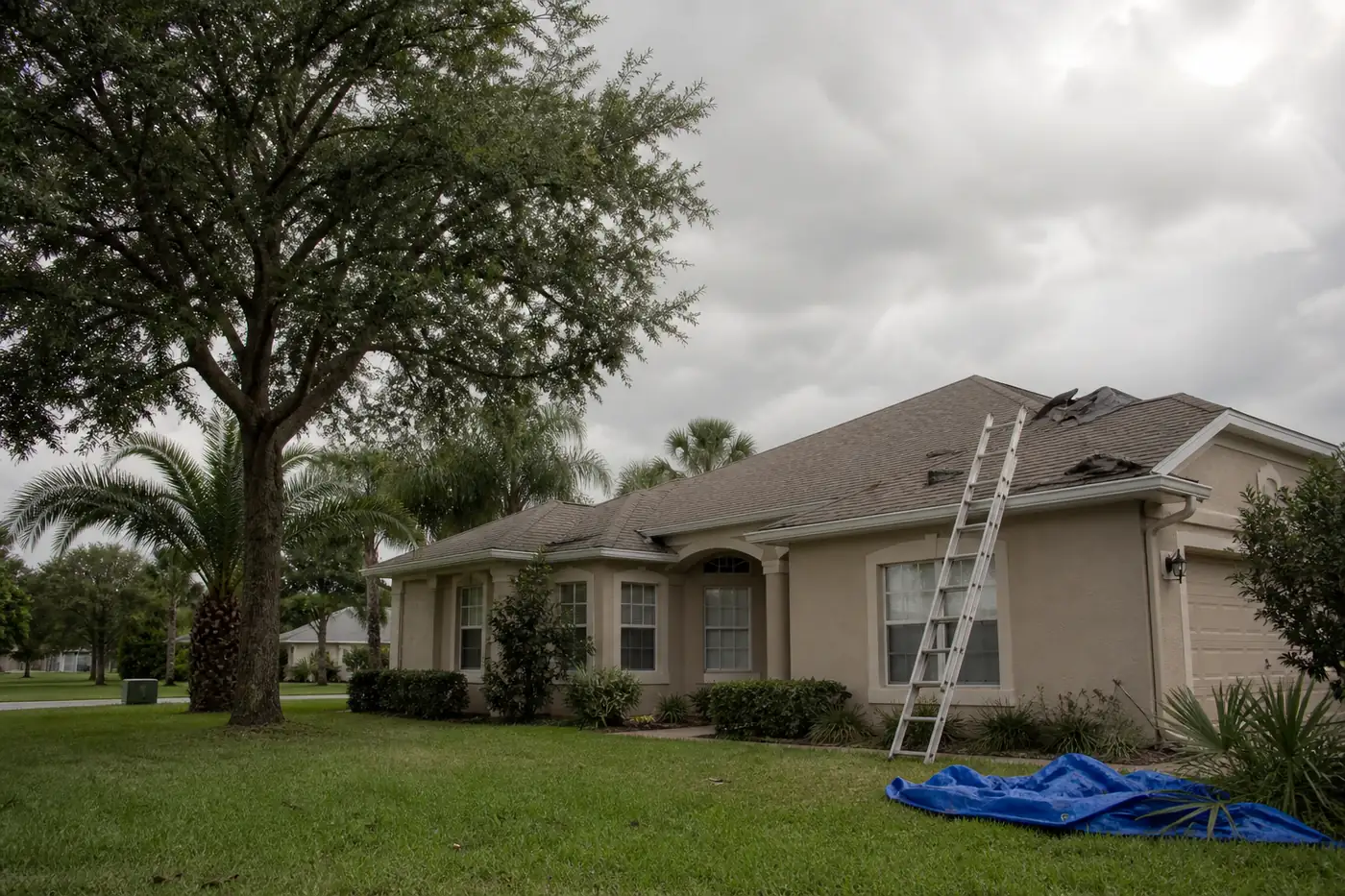A Central Florida home after a storm, with missing shingles and a ladder at the eave.